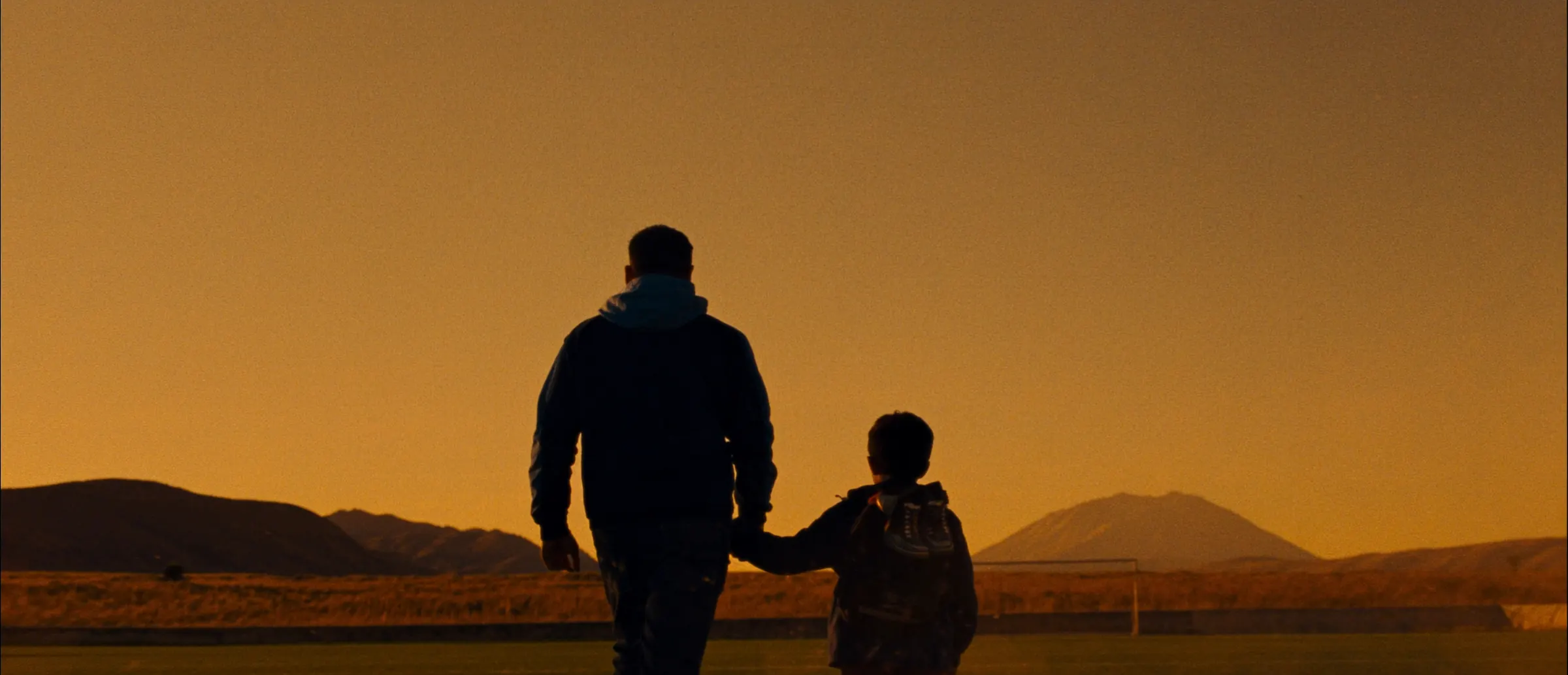 Padre e hijo caminando hacia la cancha al atardecer